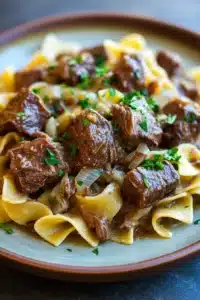 Close-up of slow cooker beef and noodles with a rich sauce and garnished with herbs.